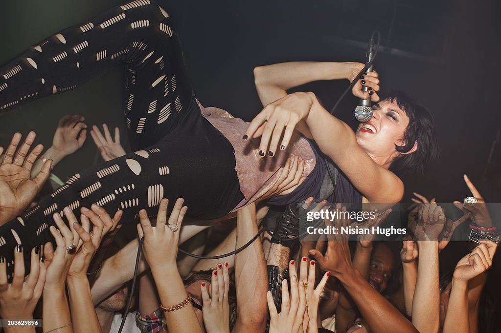 Woman singing into microphone while crowd surfing