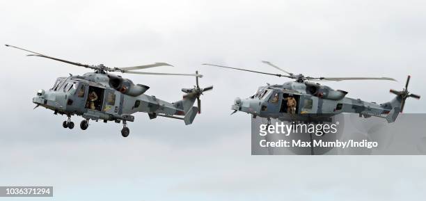 Royal Marines Commandos hang out of the open doors of two Royal Navy Wildcat Maritime Attack Helicopters as they arrive at The Royal Marines Commando...