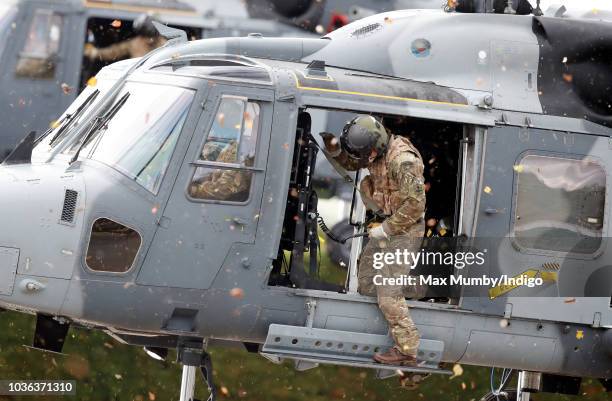 Royal Marines Commando hangs out of the open door of a Royal Navy Wildcat Maritime Attack Helicopter as it arrives at The Royal Marines Commando...