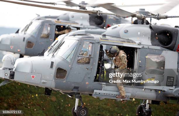 Royal Marines Commando hangs out of the open door of a Royal Navy Wildcat Maritime Attack Helicopter as it arrives at The Royal Marines Commando...