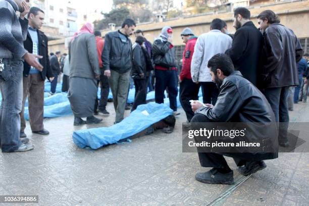 Man reads prayers for the dead next to bodies in blue plastic bags in a school courtyard while residents try to identify missing relatives in Aleppo,...