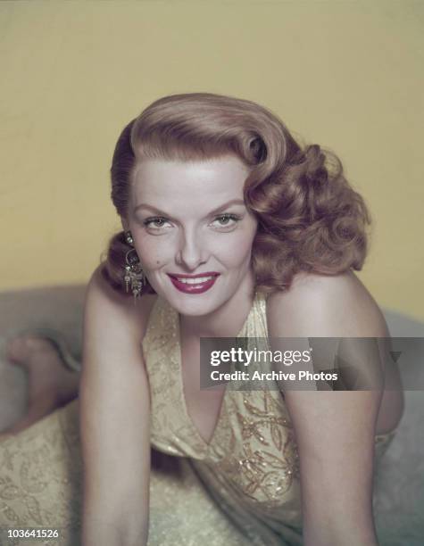 Actress Jane Russell pictured leaning forward, supported by both hands, USA, circa 1950. Russell, smiling, is wearing a yellow embroidered dress and...