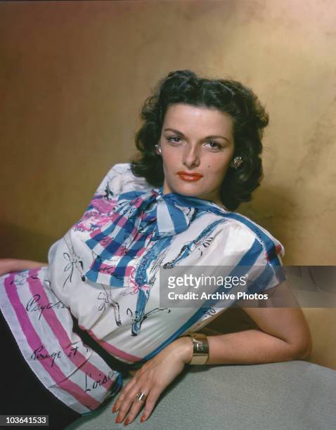 Actress Jane Russell pictured leaning back, supported by her left arm, USA, circa 1955. Russell is wearing a white, pink and blue printed top,...