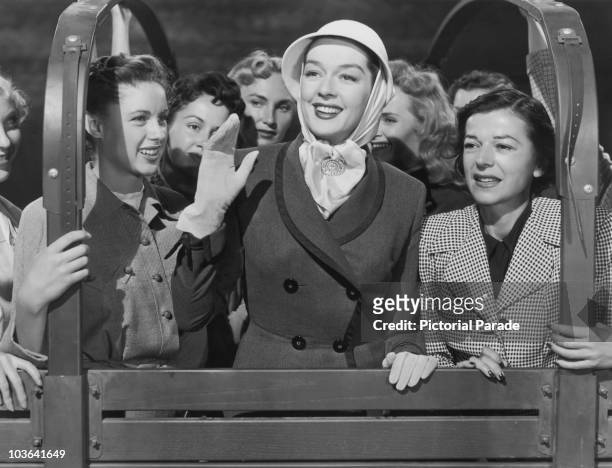 Actress Rosalind Russell pictured smiling and waving while wearing a head scarf and gloves during a film role, USA, circa 1950.