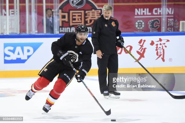 Mark Giordano of the Calgary Flames skates around head coach Bill Peters during practice at the Universiade Sports Center on September 14, 2018 in...