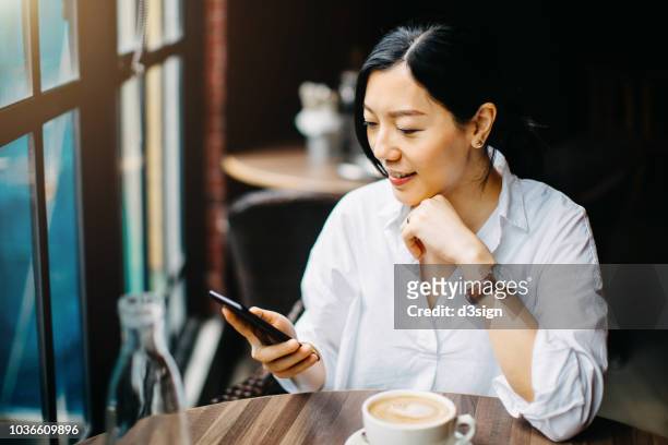 young businesswoman reading news on smartphone and drinking coffee in cafe in the morning - true peoples celebration day one stock pictures, royalty-free photos & images