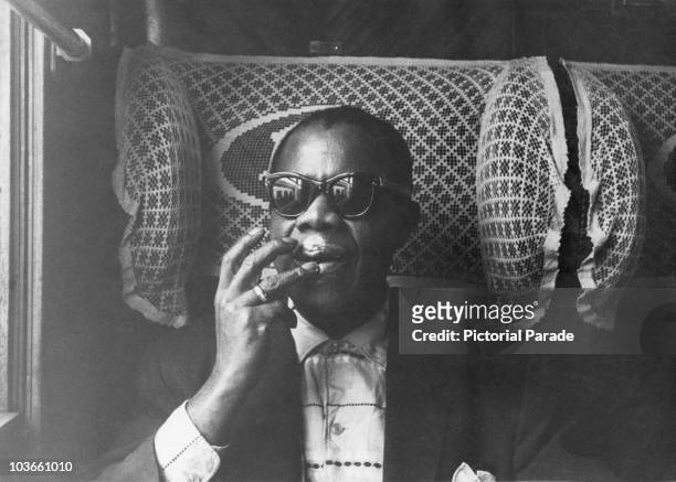 Jazz trumpeter and singer Louis Armstrong pictured moisturizing his lips while travelling on a train during his tour of France, November 1955. Also...