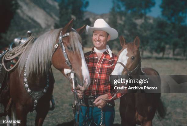 Country and western singer Gene Autry , dressed in cowboy hat and plaid shirt, poses with two horses, USA, circa 1955. Autry gained fame as 'The...