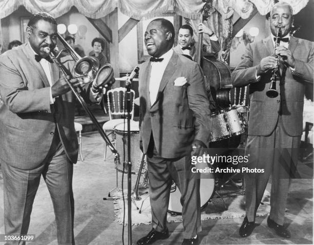 Jazz trumpeter and singer Louis Armstrong pictured performing with a band, USA, circa 1960. Armstrong is singing, with his trumpet at his side, and...