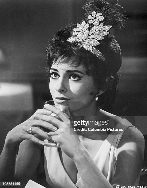 Headshot of actress Elizabeth Ashley pictured wearing a feather headdress, and holding a glass of brandy to her lips, in a scene from the film, 'Ship...