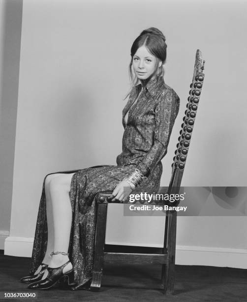 English actress Sarah Miles pictured wearing a full length shirt dress that she designed herself, seated in a high backed wooden chair in England on...