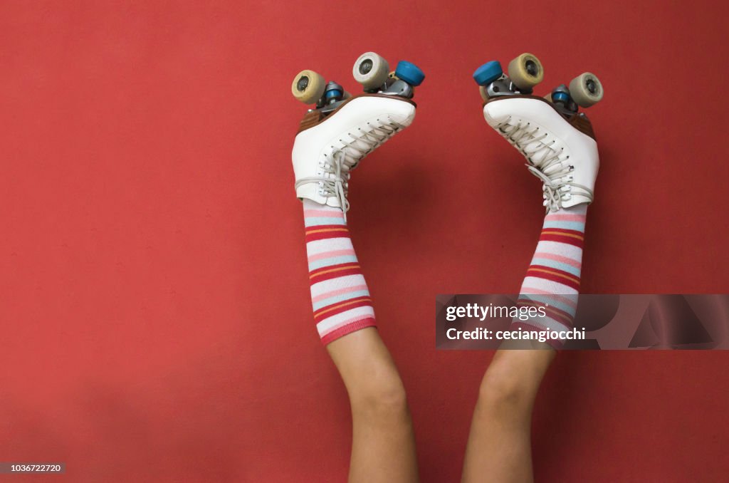 Girl's legs wearing long socks and rollerskates upside down against a wall