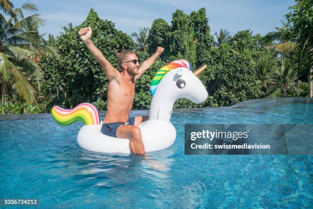 junger mann auf aufblasbaren einhorn, spaß im pool des hotels sitzen auf aufblasbaren spielzeug ausgestreckten für freiheit und positivität menschen urlaub reisekonzept - einhorn wald stock-fotos und bilder