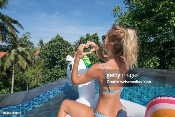 mädchen auf aufblasbaren einhorn in ein unendlich schwimmbad machen einen herz form finger liebevolle urlaub und sommer umrahmen. die leute reisen spaß glück konzept - einhorn wald stock-fotos und bilder