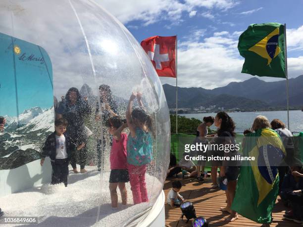 Children play in a giant walk-in snow globe on the grounds of the House of Switzerland which attracts up to 10,000 visitors every day in Rio de...