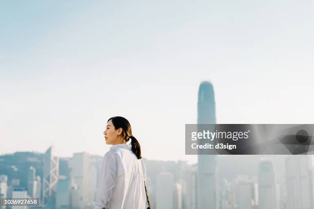confident young asian woman standing against hong kong city skyline and looking the way forward - asian woman smiling sunrise ストックフォトと画像