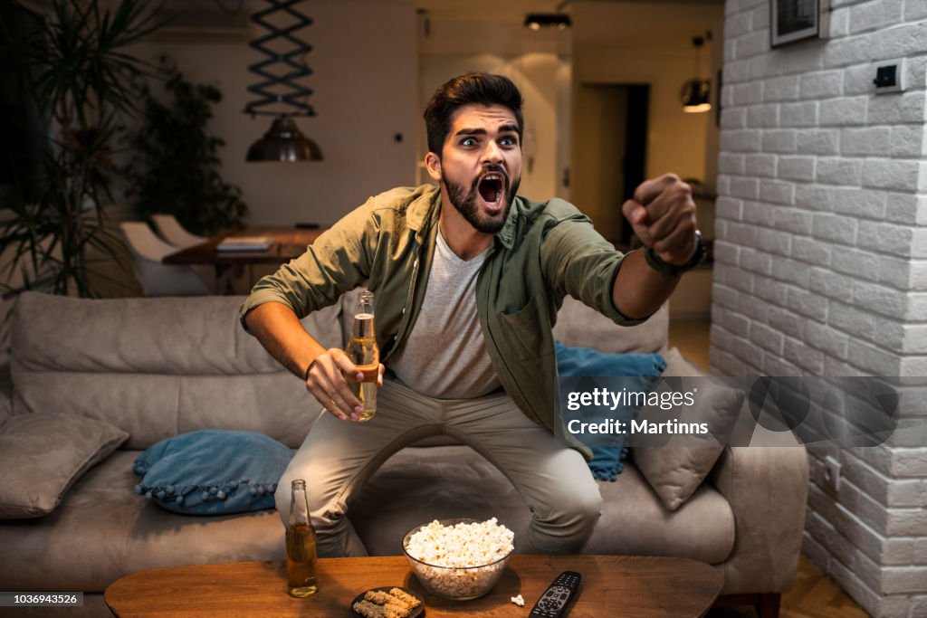 The young man is watching a sports game on TV