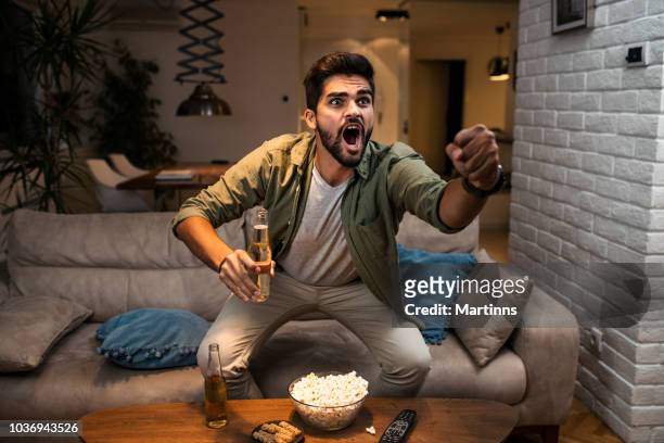 the young man is watching a sports game on tv - match sport imagens e fotografias de stock