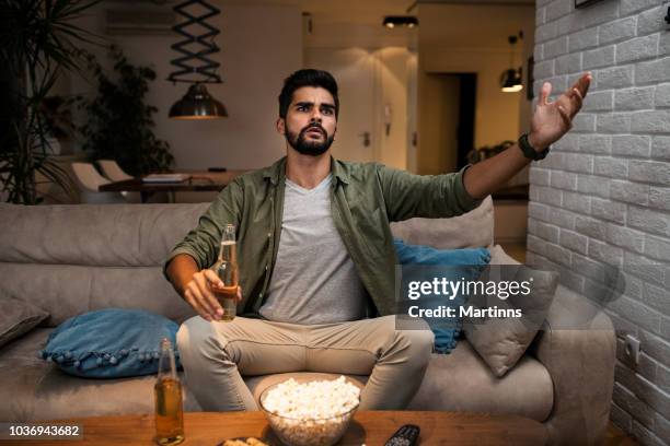 the young man is watching a sports game on tv - sports man cave stock pictures, royalty-free photos & images