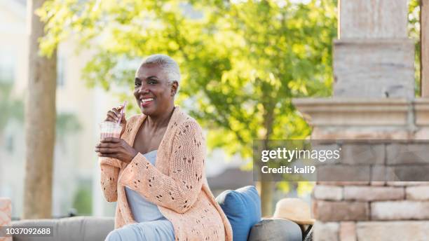 senior afroamerikanerin entspannend auf terrasse - mature woman smoothie stock-fotos und bilder