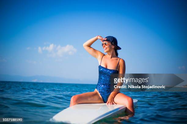 woman in blueswimsuit sitting on a surfboard - woman surfing stock pictures, royalty-free photos & images
