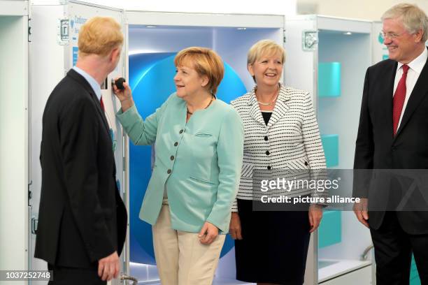 German Chancellor Angela Merkel presses a button in an exhibition as she stands next to Premier of North Rhine-Westphalia Hannelore Kraft , CEO of...
