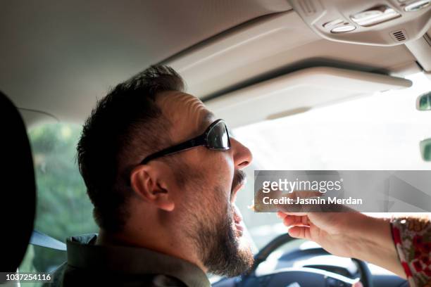 man driving car and eating food - snacking on the go stock-fotos und bilder