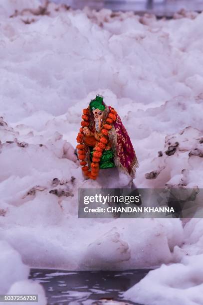 Young Indian boy immerses an idol of the Hindu god Lord Ganesh in the polluted Yamuna river on the ninth day of the eleven-day long festival Ganesh...