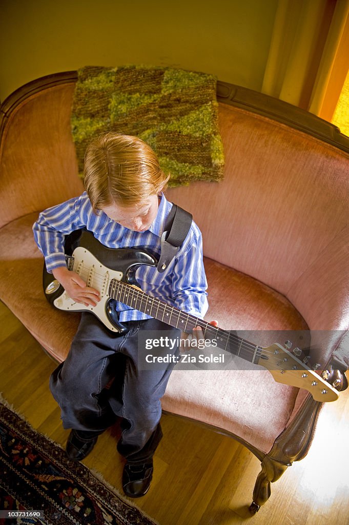 Boy on couch with his black electric guitar