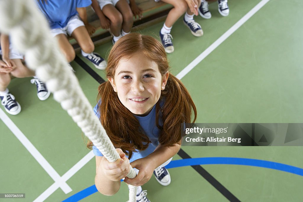 Girl starting to climb rope in gymnasium