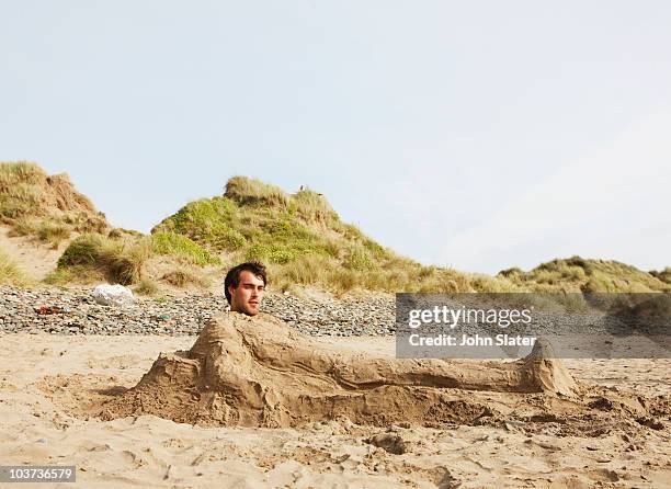 man buried in sand at beach - buried in sand stock-fotos und bilder