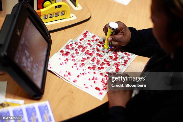Player marks her number on a bingo card, next to an electronic bingo screen at a Gala Bingo club, operated by Gala Coral Group Ltd., in London, U.K.,...