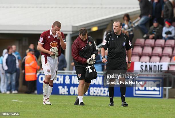 Andy Holt of Northampton Town leaves the pitch with physio Stuart Barker as referee Carl Boyeson looks on during the npower LeagueTwo match between...