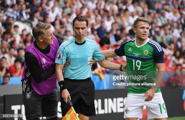 Germany's Bastian Schweinsteiger and Northern Ireland's Jamie Ward help assistant referee Frederic Cano from France after he was hit by a ball into...