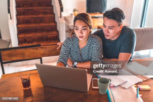 coppia seria che usa il laptop mentre è seduta a casa - couple looking laptop foto e immagini stock