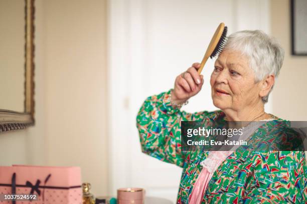 senior woman is combing her hair in the morning - comb stock pictures, royalty-free photos & images