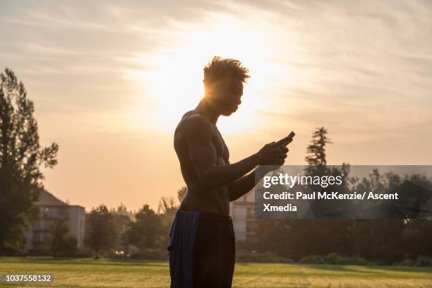 muscular young man checks text message in urban park - ew stock pictures, royalty-free photos & images