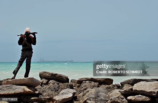 Pirate stands on a rocky outcrop on the coast in Hobyo, central Somalia, on August 20, 2010 as he looks at a hijacked Korean supertanker anchored on...