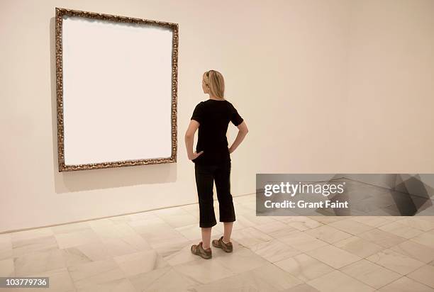 young lady looking at blank art frame. - art museum stockfoto's en -beelden