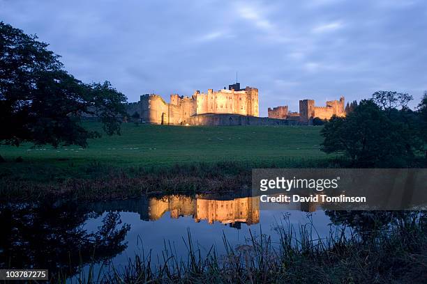 illuminated alnwick castle reflected in still waters of river aln at dusk. - alnwick castle 個照片及圖片檔