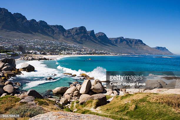 waves crashing onto camps bay beach with twelve apostles mountains in distance. - camps bay stock-fotos und bilder