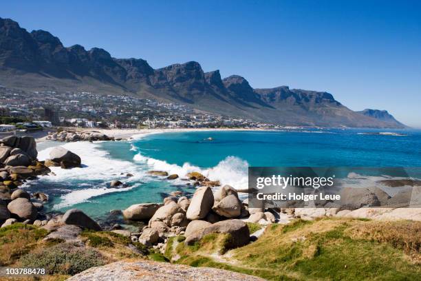 waves crashing onto camps bay beach with twelve apostles mountains in distance. - camps bay stock pictures, royalty-free photos & images
