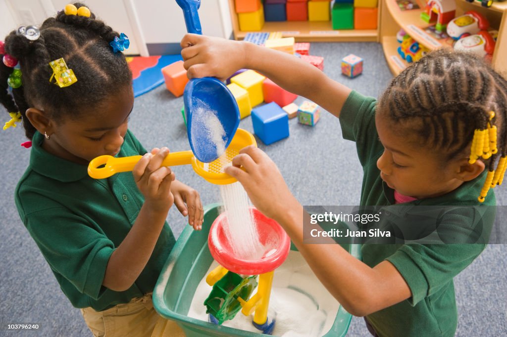 Two girls playing with sand in classroom