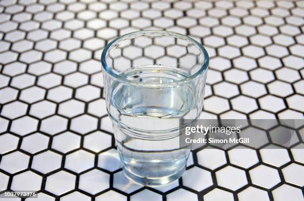 half-full water glass on a tiled table - half full stock pictures, royalty-free photos & images