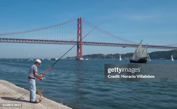 Man is seen fishing while Portuguese caravel Vera Cruz sails on the Tagus River near 25 de Abril bridge on September 22, 2018 in Lisbon, Portugal....