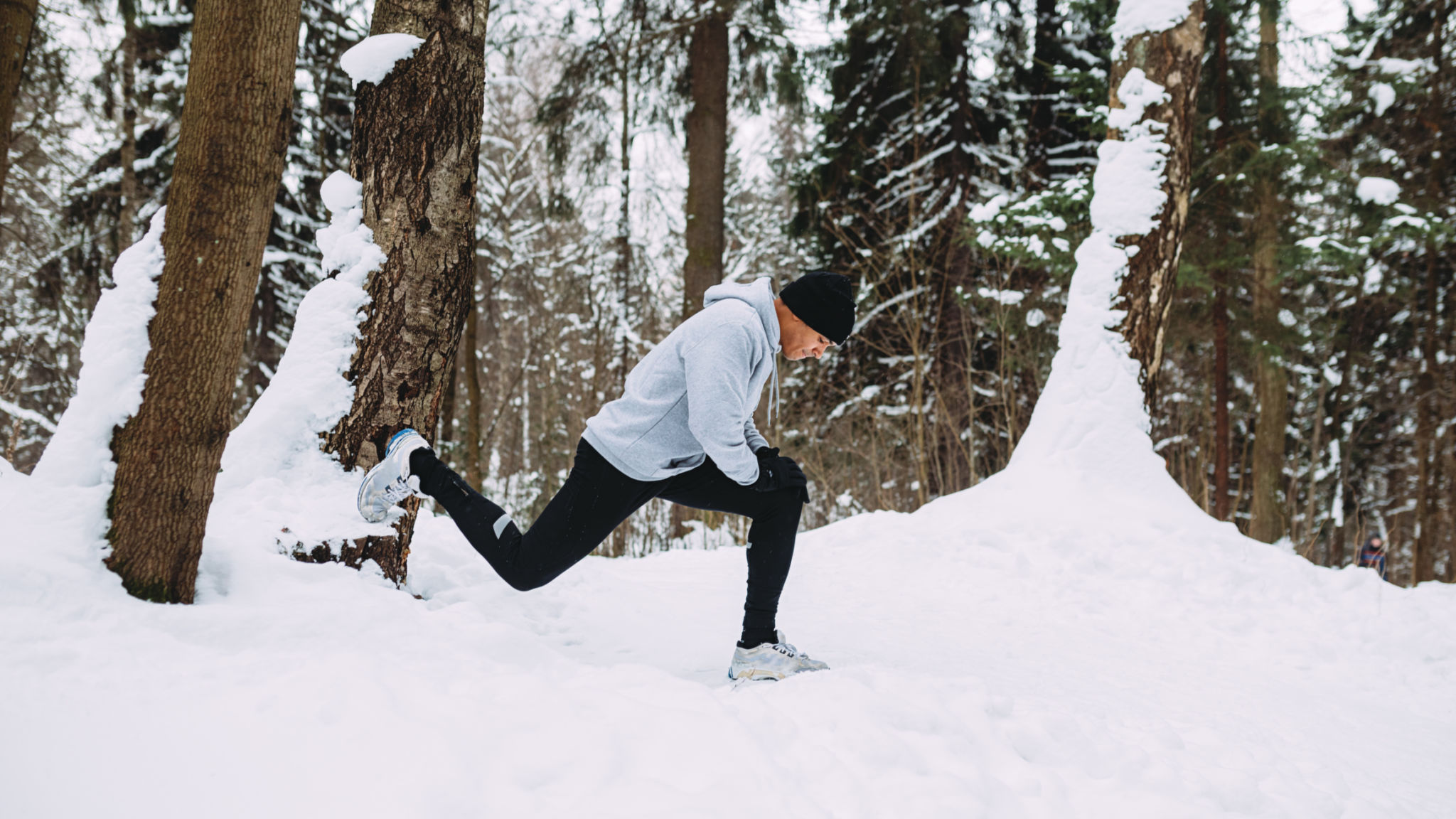 Corridore che fa esercizi di stretching in una foresta di neve Corridore che fa esercizi di stretching in una foresta di neve