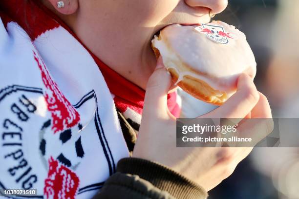 Young woman bites into a sweet pastry, in some regions known as 'Berliner', decorated with the logo of Bundesliga soccer club RB Leipzig in Leipzig,...