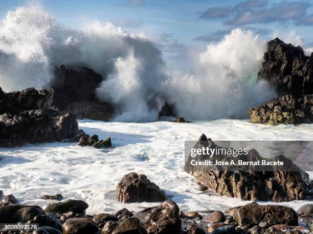crest of a wave of sea with white foam that breaks on a cliff of volcanic rocks in terceira island in the azores islands, portugal. - costa rochosa - fotografias e filmes do acervo