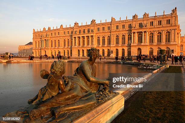 bronze statue decorating water parterres with chateau of versailles in background. - reggia di versailles foto e immagini stock