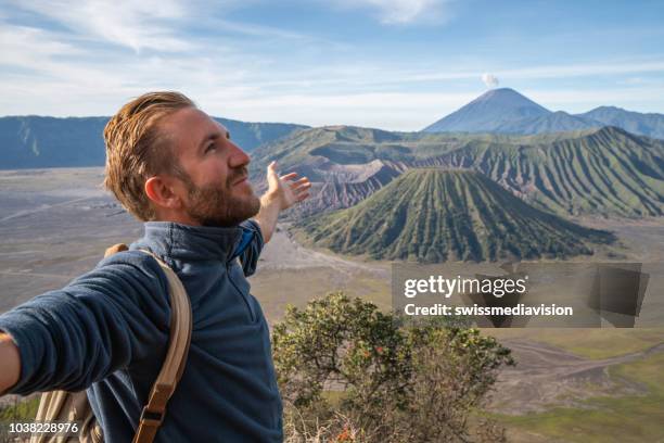 young man hiking stands arms outstretched on top of mountain with bromo volcanoes view in indonesia- people travel fun adventure concept success and achievement - java stock pictures, royalty-free photos & images